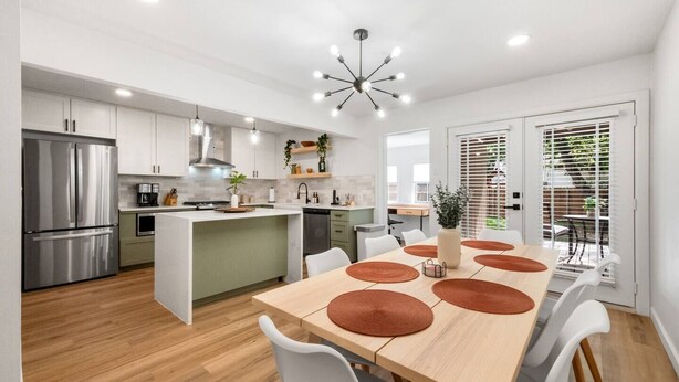 A modern kitchen with a central island, white cabinetry, stainless steel appliances, and a dining area with a wooden table and white chairs. - Ivy House / 4BR Boho Retreat Near UTD (Richardson)