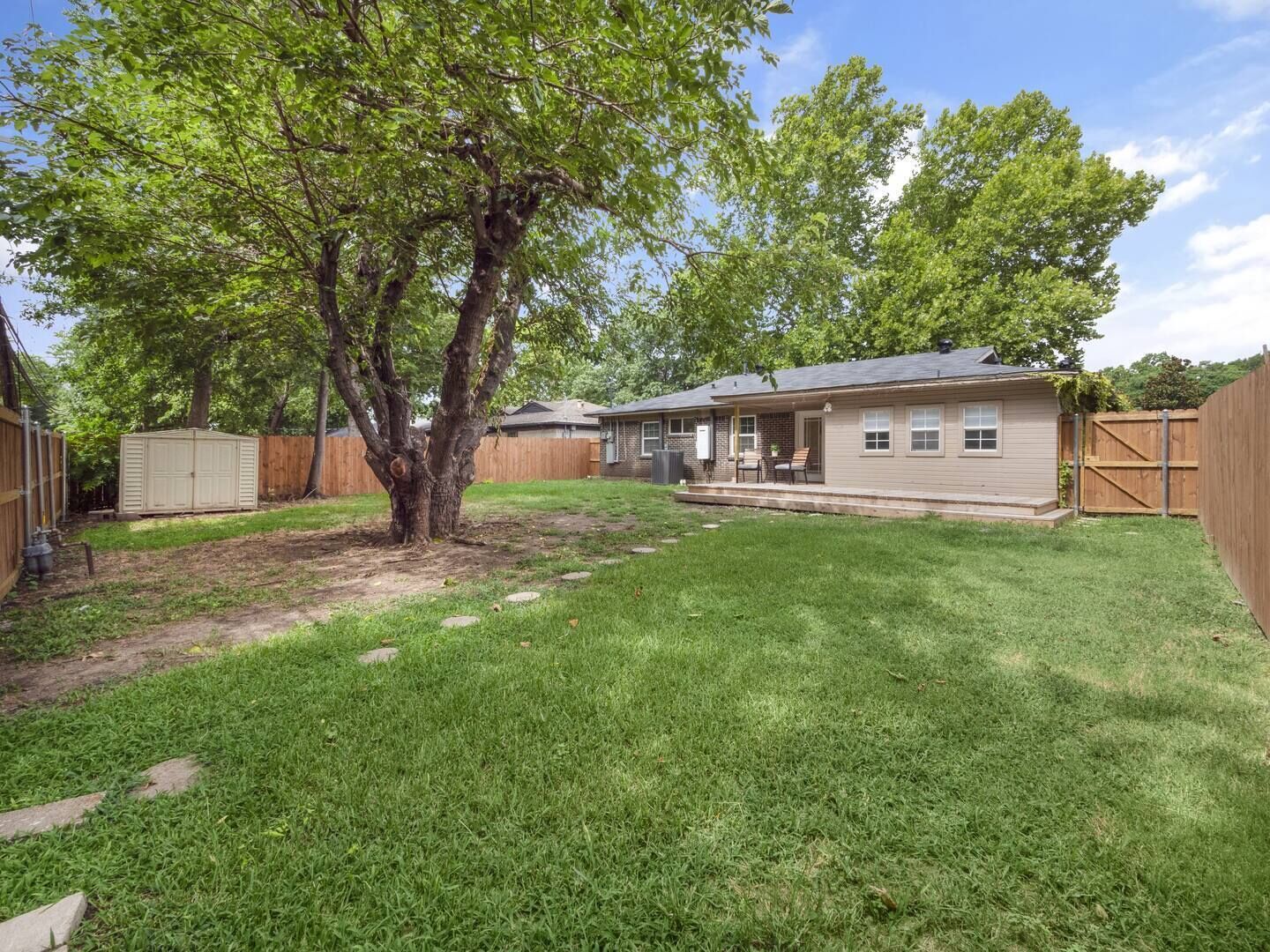 A single-story house with a covered patio, a fenced yard, and a large tree.