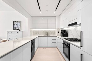 A modern kitchen with white cabinetry, a marble backsplash, and a central island. - Stylish 1 Bedroom in Binghatti Lavender JVC (Dubai)