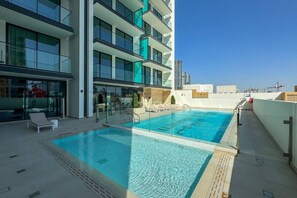 Une piscine sur le toit, avec une eau d’un bleu limpide, entourée de bâtiments modernes et surplombant un ciel dégagé.