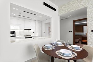 A modern dining area with a round table set for four, white walls, and a view into the kitchen.
