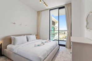 A modern hotel room with a large bed, a nightstand, a mirror, and a view of the city through a large window.