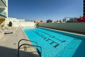 A rooftop swimming pool with lounge chairs and a view of the city skyline.