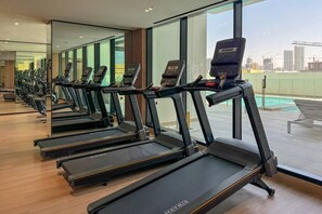 A row of treadmills in a gym with large windows and a view of a cityscape.
