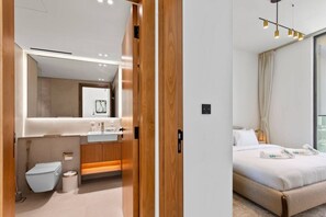 A modern hotel room with a large mirror, a wooden vanity, a bed with white bedding, and a view of the city through the window.