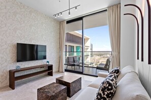 A modern living room with a flat-screen TV, a sofa, a coffee table, and a balcony with a city view.