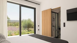 A modern bedroom with a large sliding glass door leading to a garden, a bed with a black headboard, and a wooden wardrobe.