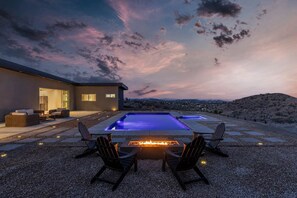 Un área de piscina moderna al aire libre con una chimenea, asientos y vistas al paisaje desértico.
