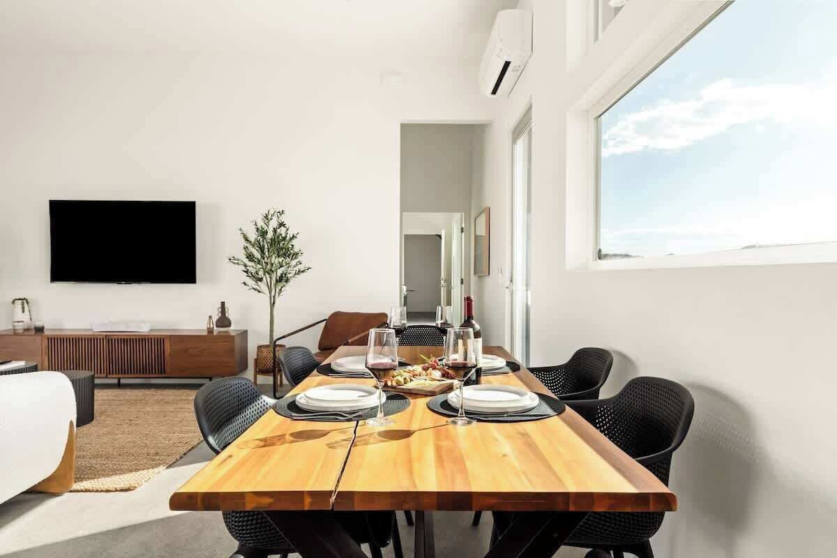 Een moderne eethoek met een houten tafel voor vier personen, omringd door zwarte stoelen. Aan de muur is een flatscreen televisie bevestigd, en er staat een potplant in de achtergrond.