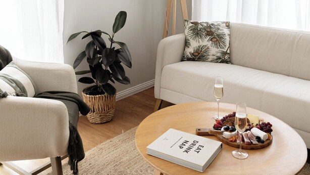 Un salon moderne avec un canapé, une table basse sur laquelle se trouvent un livre et des lunettes, une lampe et une plante.