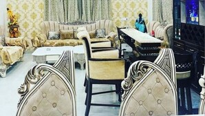 A well-lit living room with a sofa set, a dining table, and chairs. - Royal stay farm house (Gurugram)