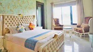 A hotel room with a large bed, two armchairs, a small table, and a window with curtains. - Royal stay farm house (Gurugram)