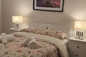 A neatly made bed with floral bedding, two bedside lamps, a framed picture above the bed, and a white nightstand with a drawer. - Dublin - 3 Bedroom Cosy Home - Sleeps Max 7 (Dublin)