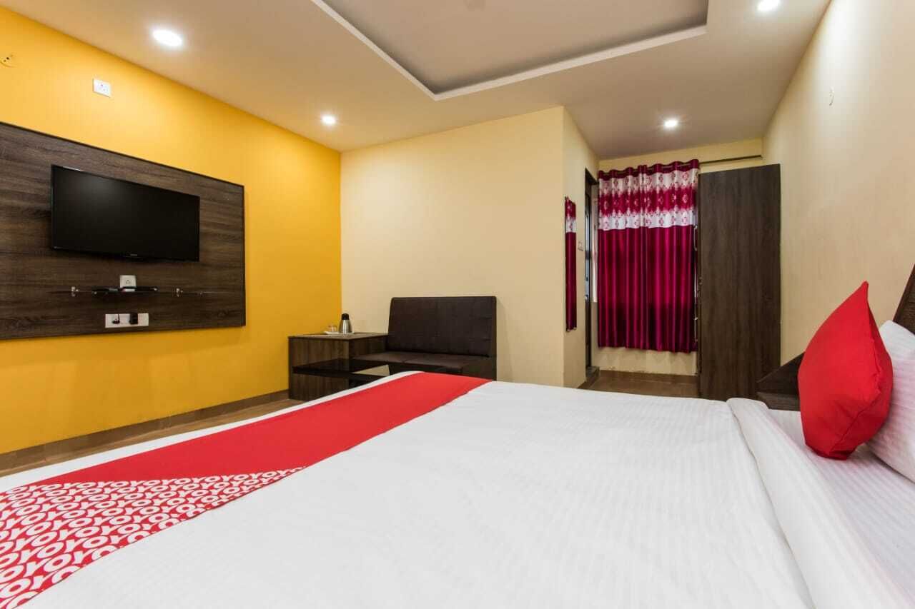 A hotel room with a large bed, a flat-screen TV mounted on the wall, a bedside table, and a red and white patterned runner.