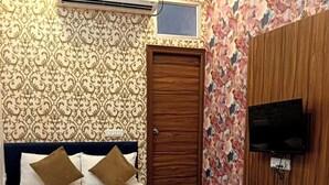 A bedroom with a bed, a wooden door, a TV mounted on the wall, and a patterned rug on the floor. - Rawla Sarkar (Udaipur)