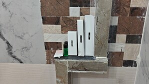 A bathroom with a tiled backsplash featuring a mix of marble and stone tiles. There are three white boxes labeled "SHAMPOO," "DEODORANT," and "SKIN CARE" on the countertop. - Rawla Sarkar (Udaipur)