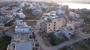 An aerial view of a residential area with multiple buildings, roads, and a river in the background. - Rawla Sarkar (Udaipur)
