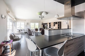 A modern kitchen with a central island, dining area with chairs, and a visible stove.