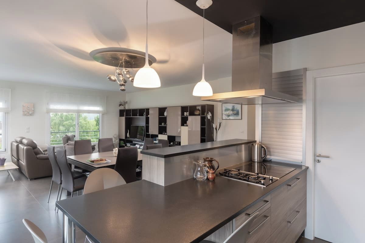 A modern kitchen with a central island, pendant lighting, and a stainless steel range hood.