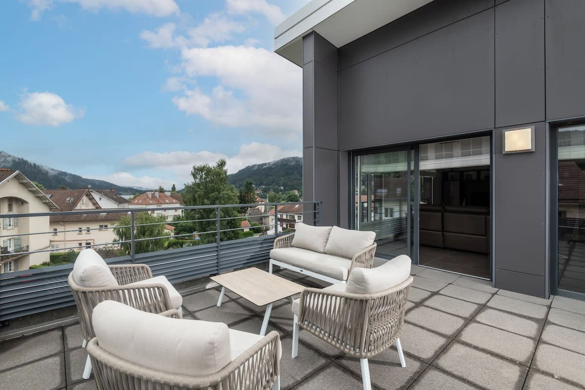 A balcony with outdoor furniture, a glass door leading to an interior space, and a view of the surrounding area.