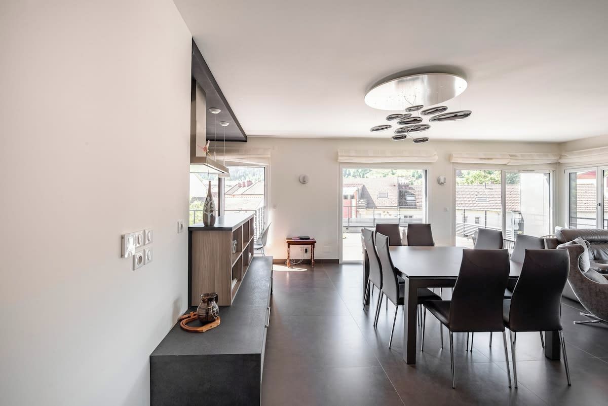A modern kitchen with a dining area, featuring a central island, dark flooring, and a contemporary light fixture.