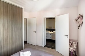 A bedroom with a bed, a wardrobe, a bathroom with a mirror, and a chair. - Appt Le Parme - Cœur de la ville - Proche lac (Gérardmer)
