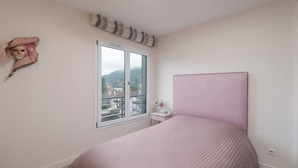 Een slaapkamer met een enkel bed, een raam met uitzicht, een nachtkastje en een decoratief object aan de muur.