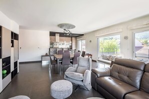 A modern living space with a dining area, a sofa, and a kitchen in the background. - Appt Le Parme - Cœur de la ville - Proche lac (Gérardmer)