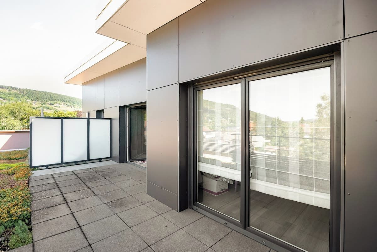 Ein modernes Gebäude mit Balkon, großen Schiebegläsern und Blick auf Grünflächen.