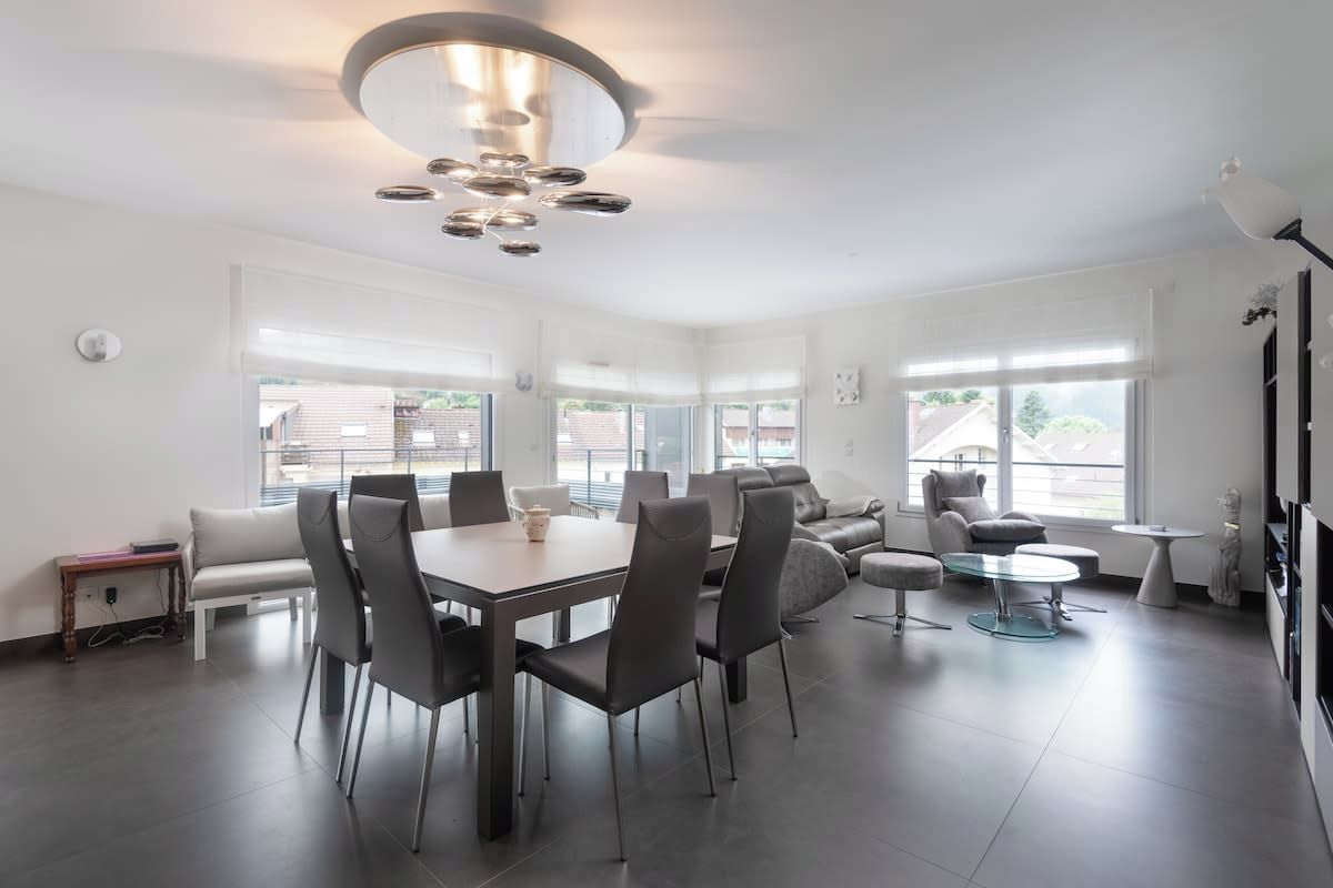 Ein modernes Wohnzimmer mit Essbereich, großen Fenstern und einer zeitgemäßen Pendelleuchte.