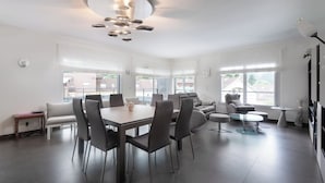 Een moderne woonkamer met een eethoek, grote ramen en een eigentijdse kroonluchter.