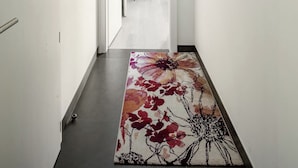 Een gang met een deur naar een kamer, een lijst met een foto aan de muur en een tapijt met bloemenprint op de vloer.