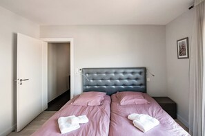 A bedroom with two beds, a door, a light switch, and a framed picture on the wall.