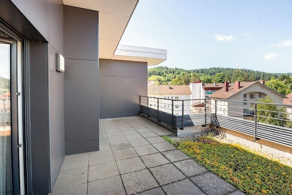 A balcony with a view of a residential area and a forested hill.