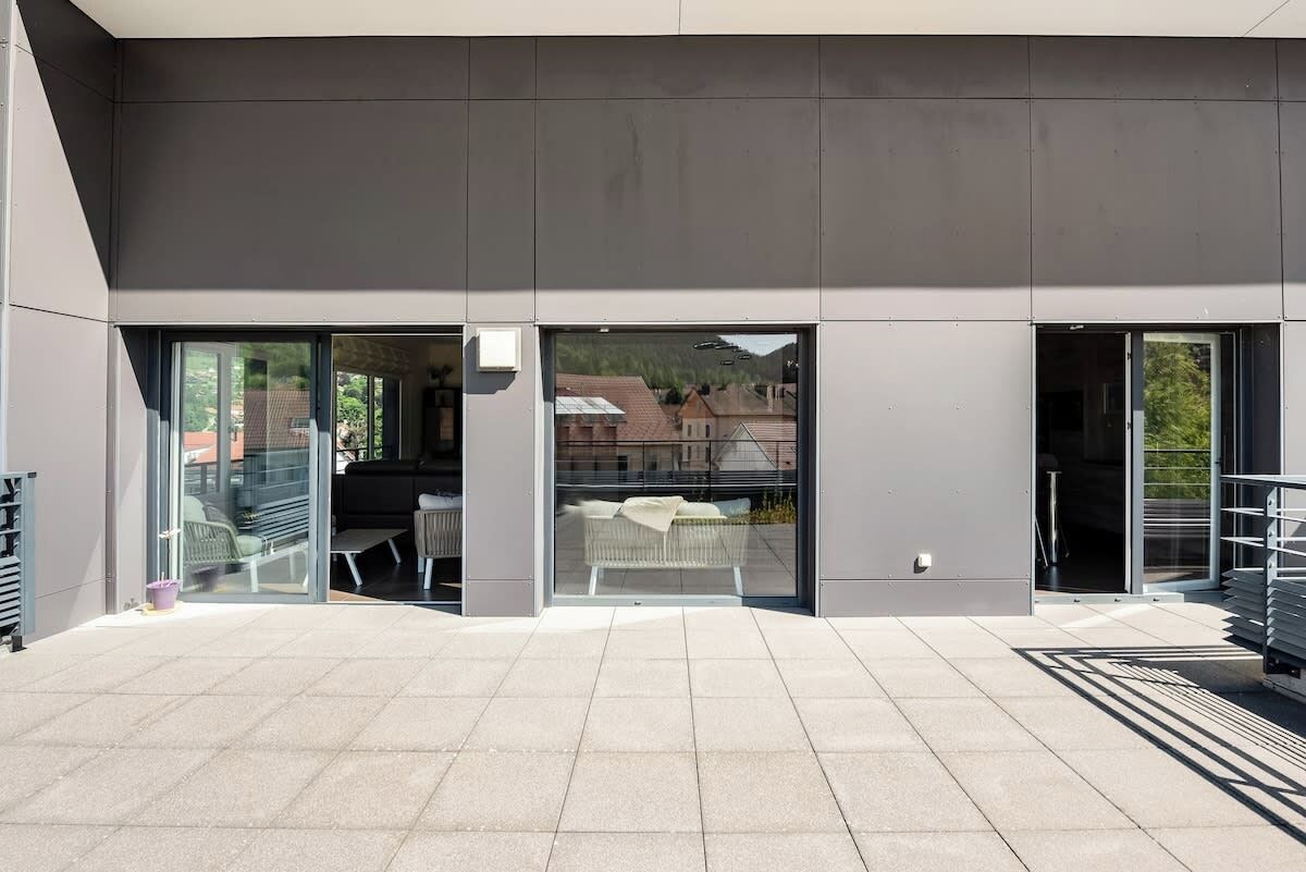 A modern building with large glass doors, a flat roof, and a paved outdoor area.