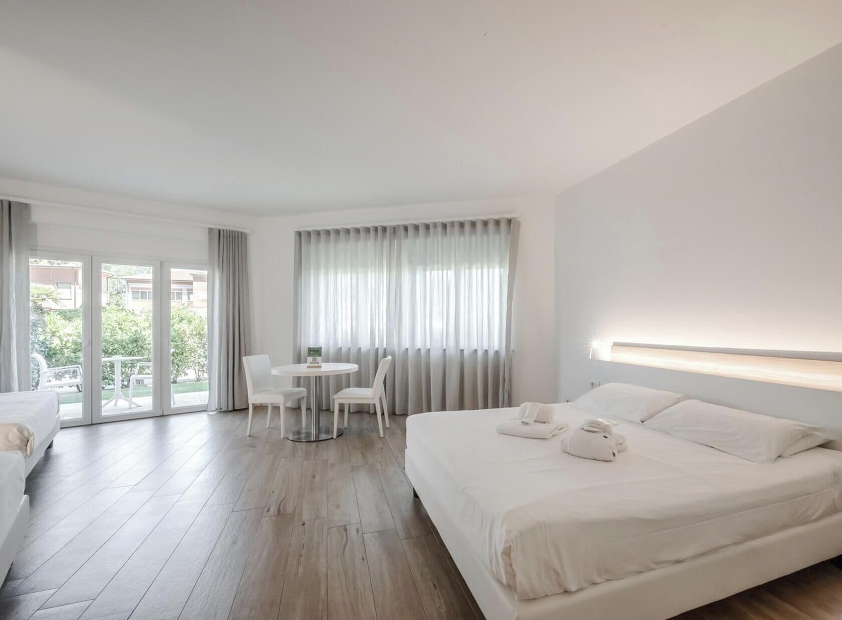 Una habitación de hotel con una cama, una mesa redonda con sillas y un balcón con cortinas.