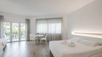 Una habitación de hotel con una cama, una mesa redonda con sillas y un balcón con cortinas.