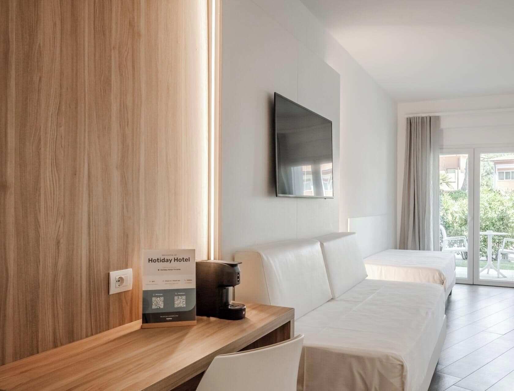Ein Hotelzimmer mit Schreibtisch aus Holz, einem Bett, einer Kaffeemaschine, einem Flachbildfernseher und einem Balkon mit Blick.