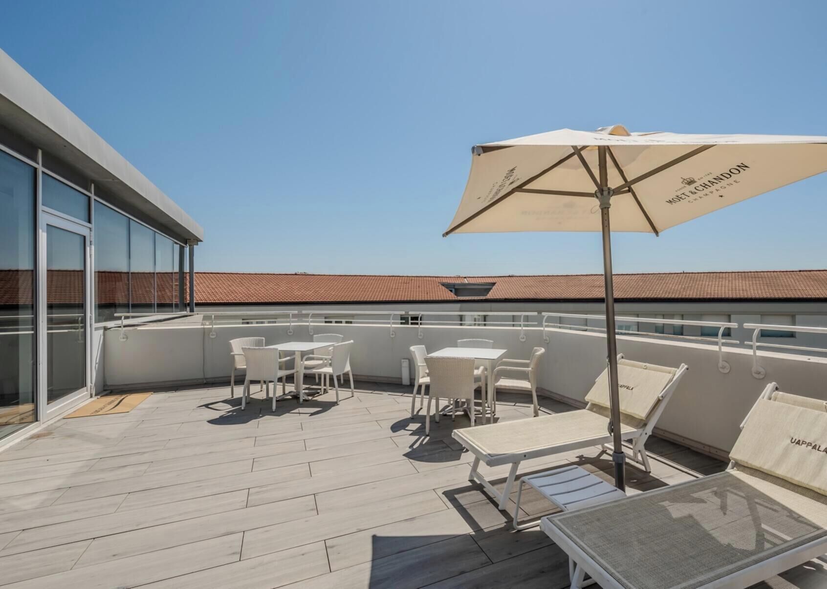 Una terraza en la azotea con mobiliario exterior, incluyendo mesas y sillas, y una sombrilla grande.