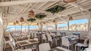 An outdoor restaurant with white tables and chairs, hanging plants, and a view of the beach. - Hotiday Room Collection - Tirrenia (Pisa)