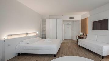 A modern hotel room with a bed, a seating area, a wardrobe, and a television.
