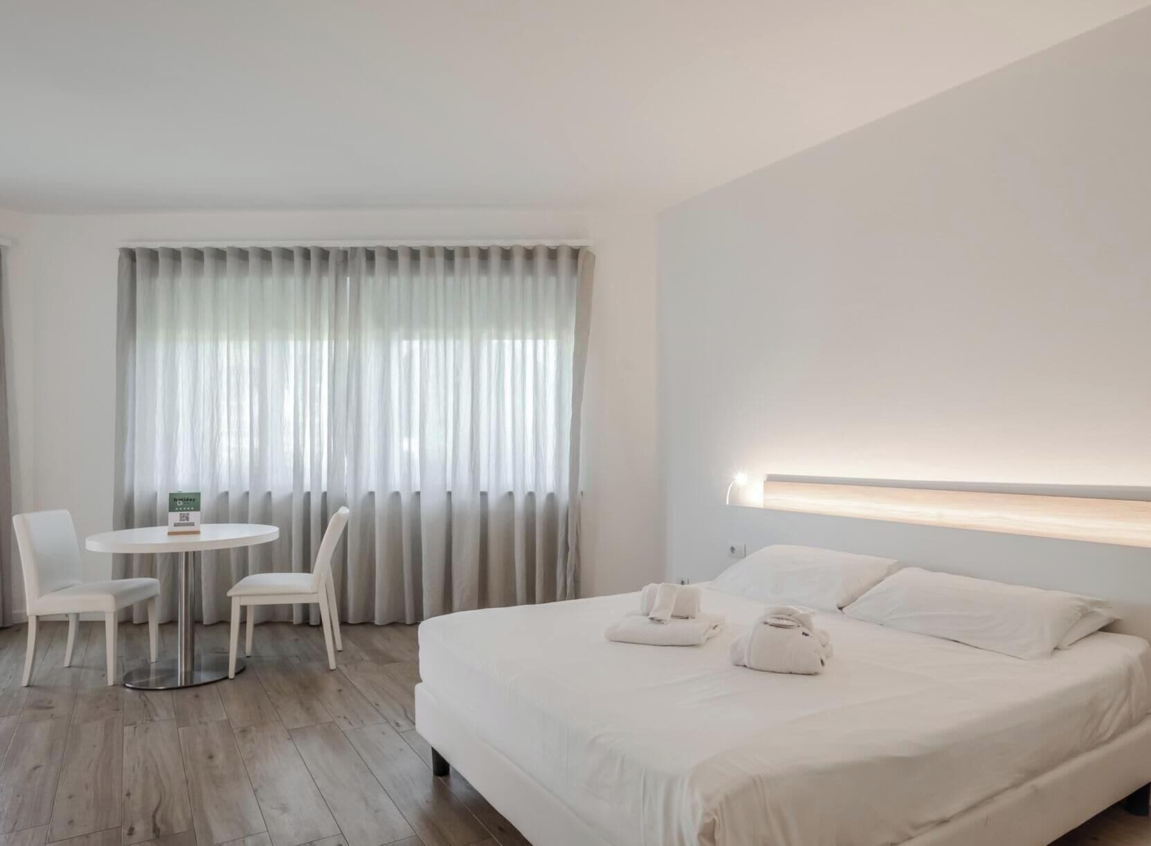 Ein Hotelzimmer mit einem Bett, einem runden Tisch mit Stühlen und einem großen Fenster mit Vorhängen.