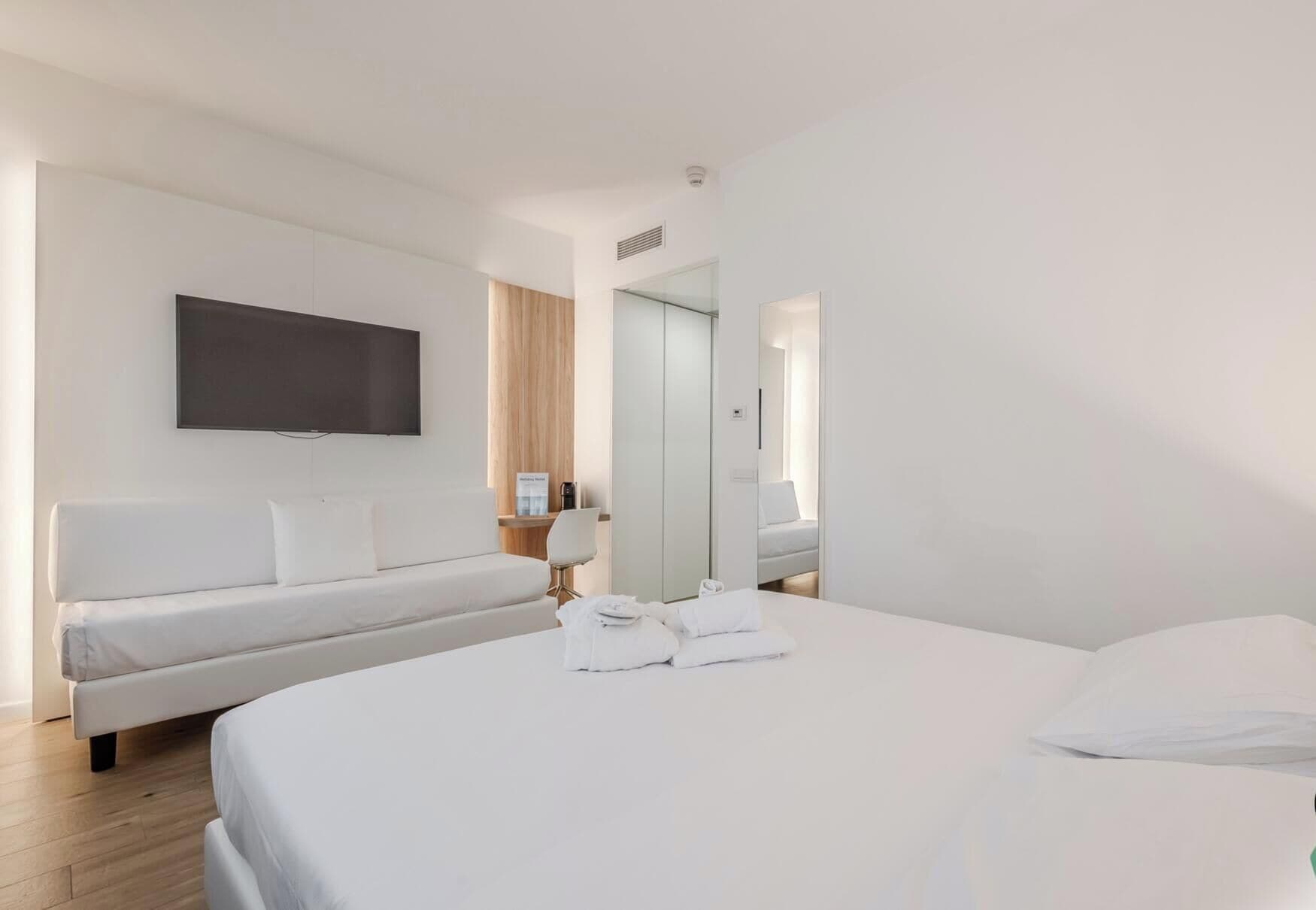 Ein Hotelzimmer mit einem Bett, einem Sofa, einem Flachbildfernseher, einem Spiegel und einem kleinen Tisch mit einer Lampe.