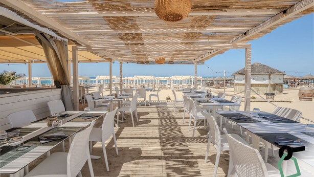 An outdoor dining area with white chairs and tables, a wooden deck, and a view of the beach and ocean. - Hotiday Room Collection - Tirrenia (Pisa)