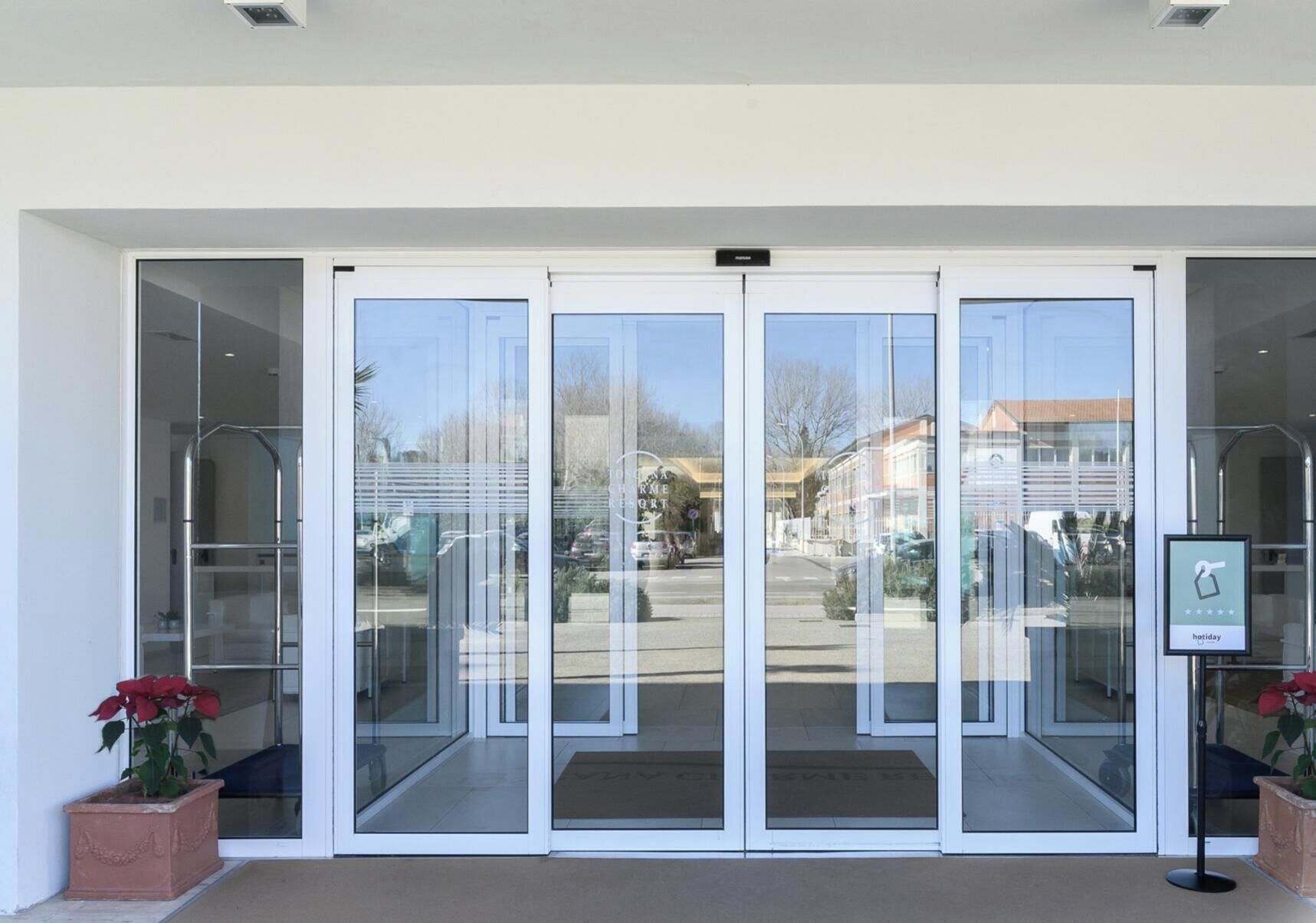 Conjunto de puertas de vidrio giratorias que dan acceso a un edificio, con vista despejada a la calle y automóviles estacionados afuera.