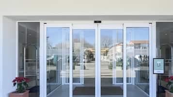 Conjunto de puertas de vidrio giratorias que dan acceso a un edificio, con vista despejada a la calle y automóviles estacionados afuera.