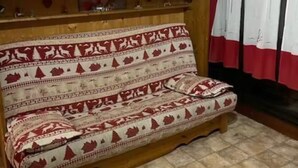 A wooden bench with heart-shaped cutouts, a patterned cushion, and a window with red curtains.