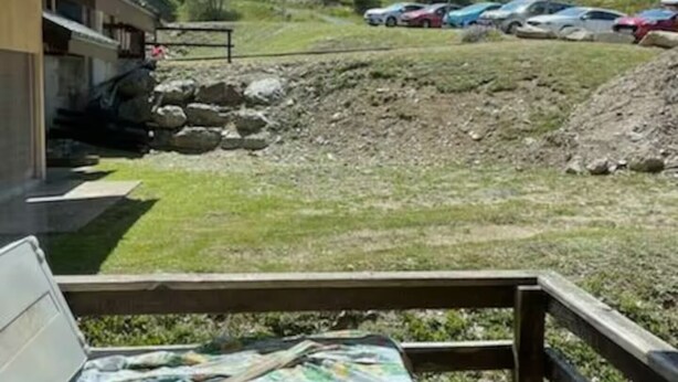 A view of a hotel with a parking area, outdoor seating, and a mountainous backdrop.