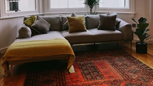 Une pièce d’angle avec un canapé, un tapis à motifs et une plante en pot.
