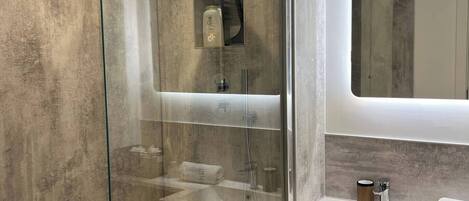 Ein modernes Badezimmer mit einer Glastrennwand zur Dusche, einem Waschtisch mit Spiegel und einem Waschbecken.